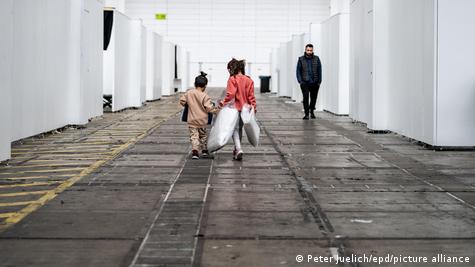 Franfurt Fuar Alanı'nda, sığınmacıların barınması için oluşturulan yerde iki çocuk ve karşıdan gelen bir yetişkin