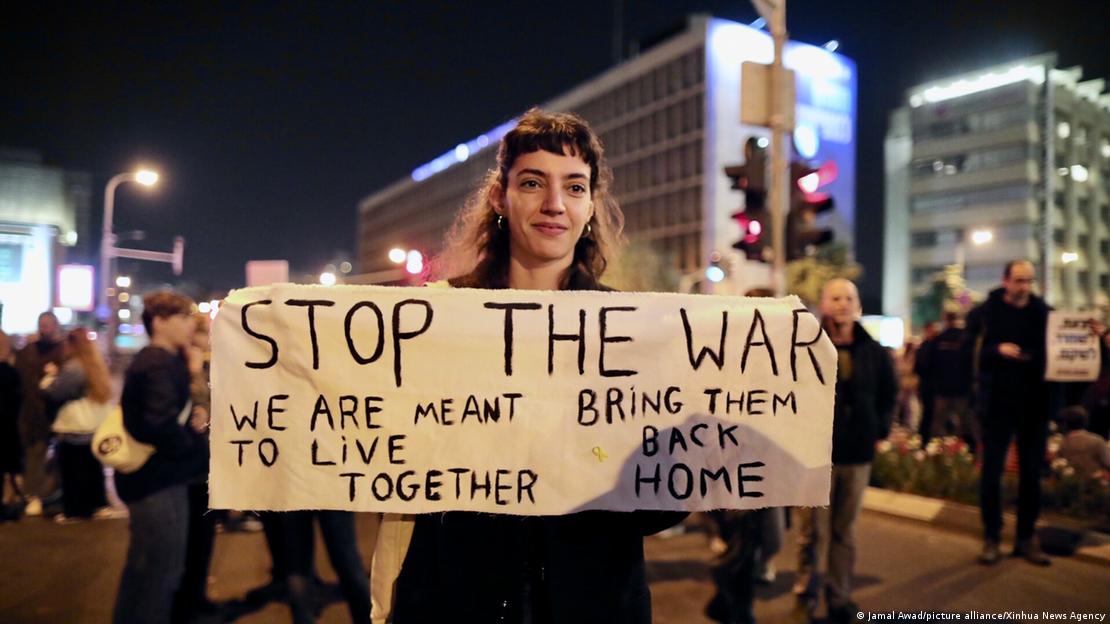Tel Aviv'deki protesto gösterisinden "Savaşı durdur" yazılı pankart açan kadın bir gösterici 